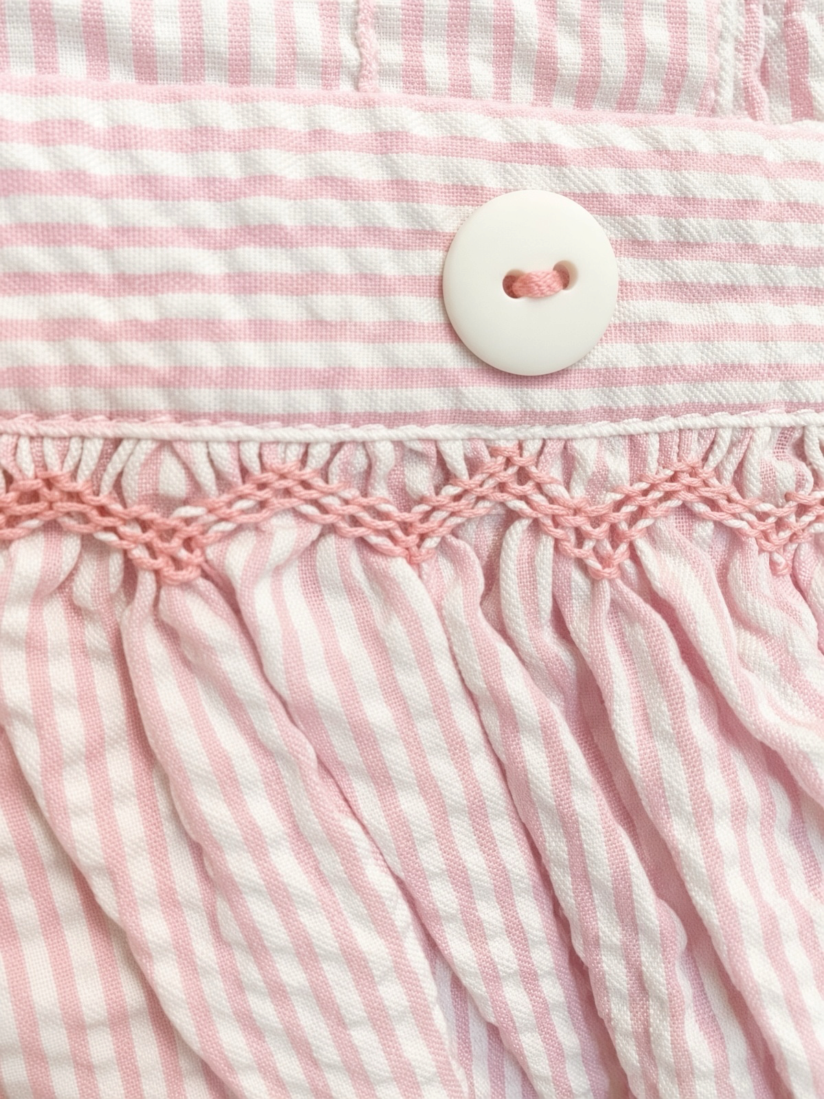 Detail of the pink hand-smocking and scalloped edge at the pinafore waistband