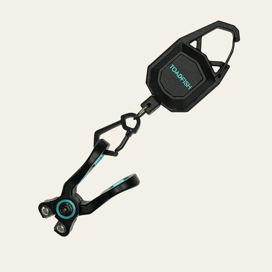 Toadfish stainless line nippers attached to a black retractable clip with carabiner, teal accents on the jaws and pivot