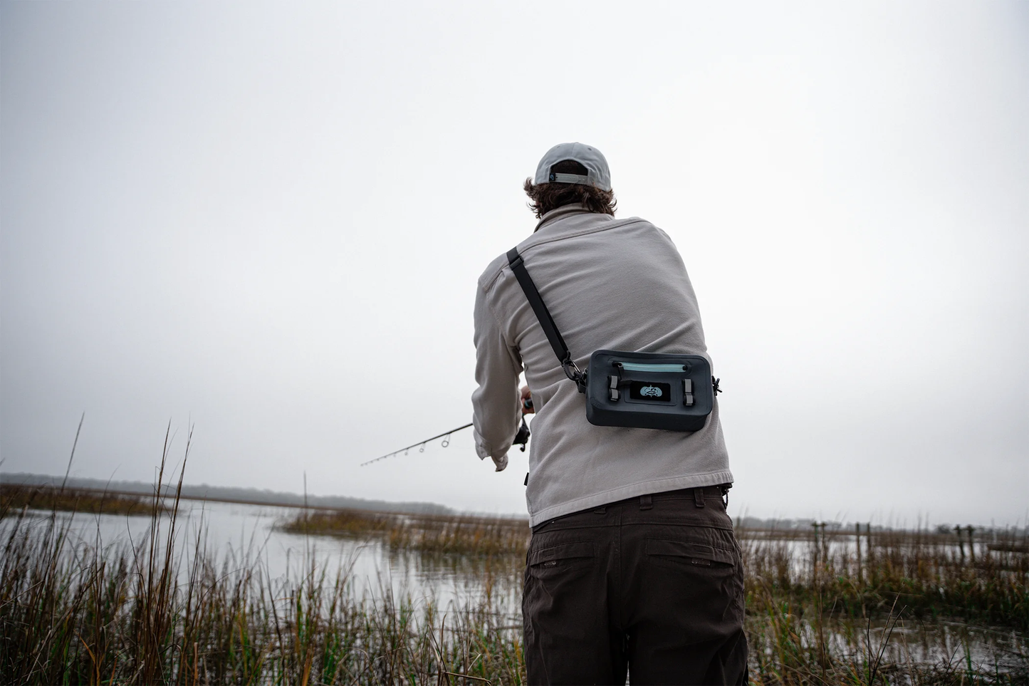 Angler wearing the Ocean Blue Toadfish Sealed Sling across his back while fishing a marsh flat on a grey morning