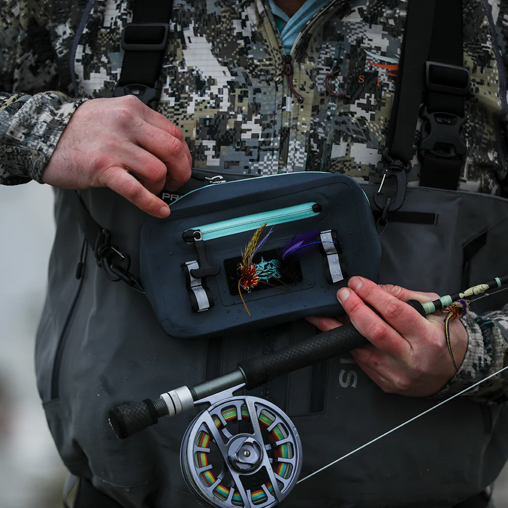 Fly angler in waders selecting flies stored on the loop panel of the Ocean Blue Toadfish Sealed Sling