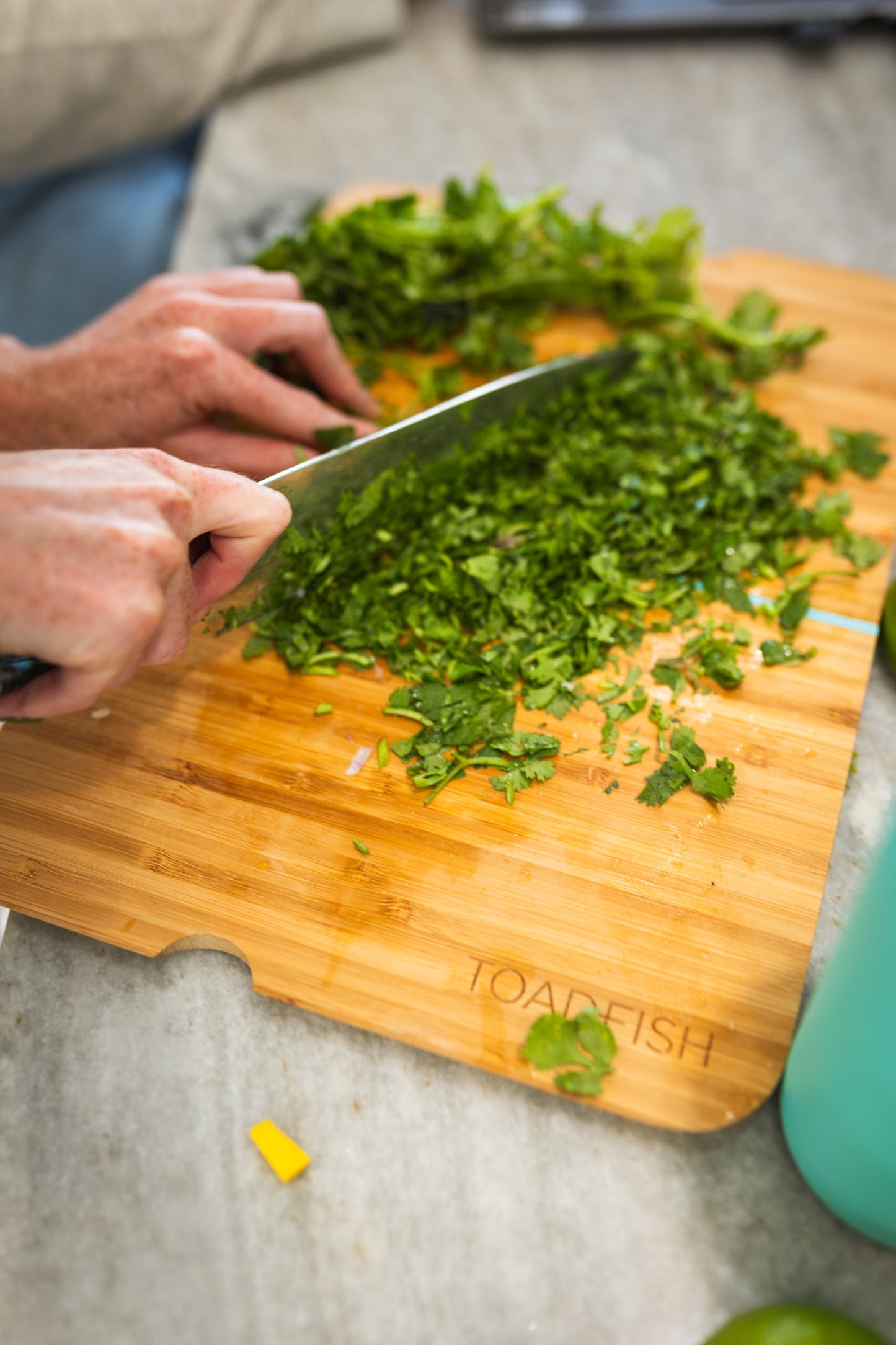 Chopping fresh cilantro with a chef's knife on the Toadfish bamboo cutting board, brand engraved in the corner